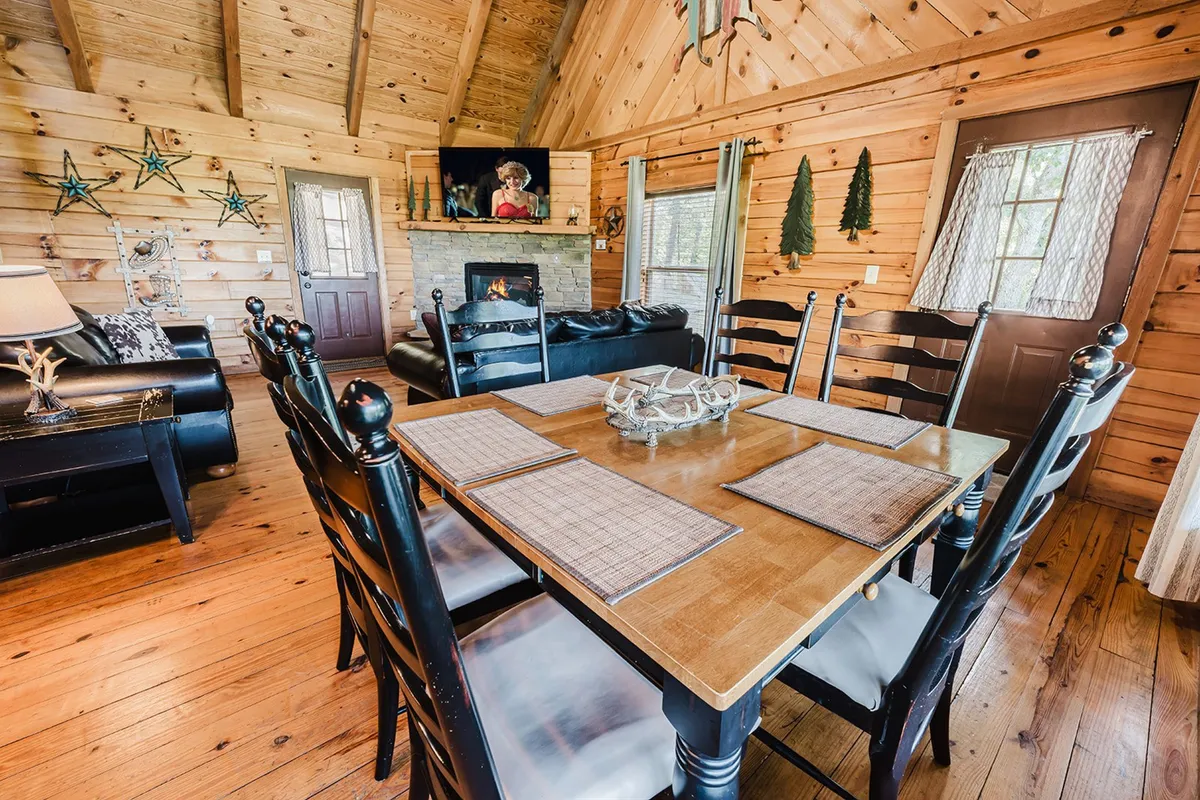 This image captures a spacious and welcoming living area with a large dining table, a cozy sofa, a glowing fireplace, and decorative accents like wall art and stars. The space feels inviting and well-suited for group activities such as shared meals, game nights, and conversations.