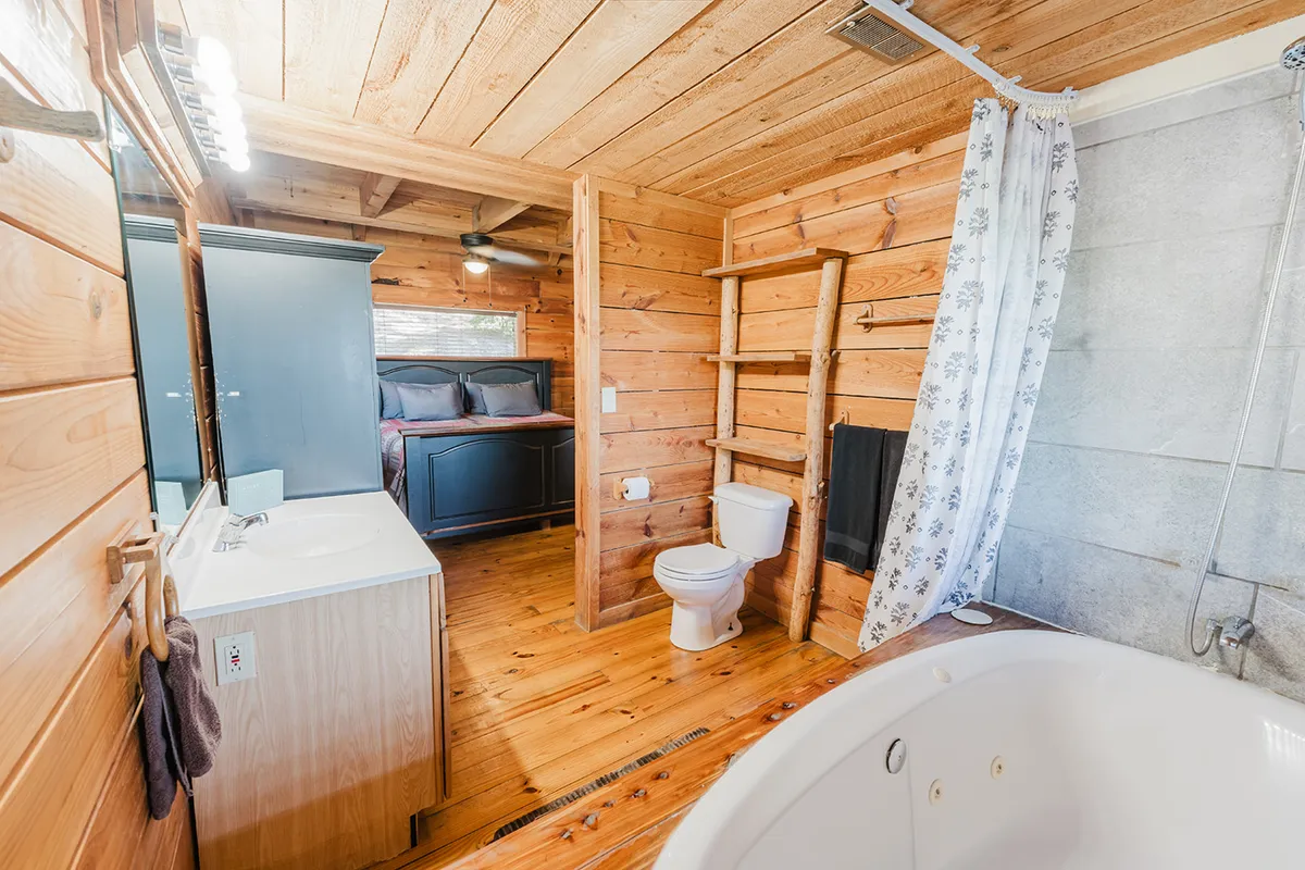 This serene bathroom scene displays a spacious bathtub beneath a wooden ceiling, with soft morning light streaming through a nearby window. The space offers a peaceful retreat for relaxing soaks, with a view into the adjacent bedroom adding to the sense of comfort and privacy.