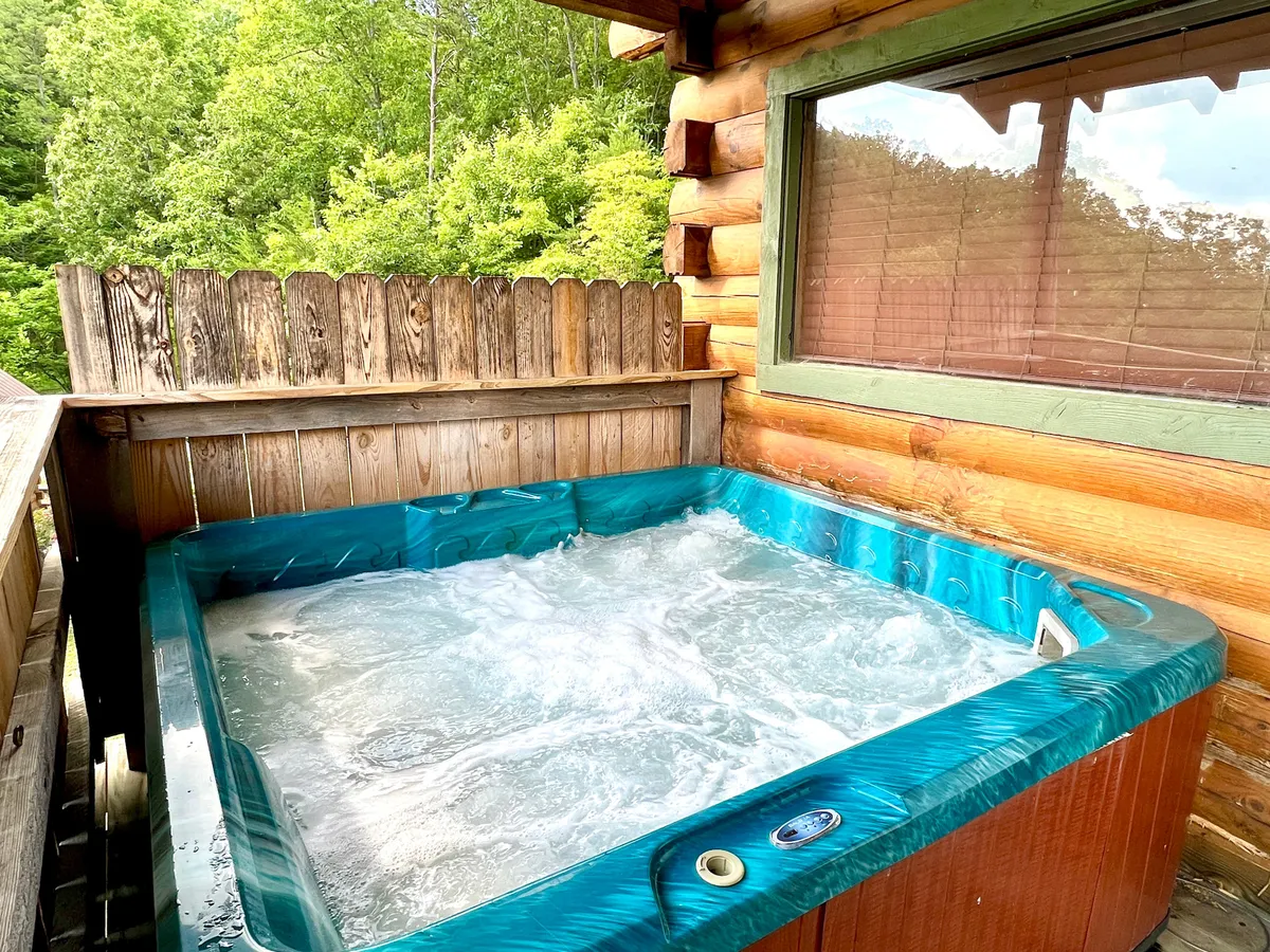 A private hot tub sits outdoors, surrounded by a wooden fence and lush greenery. The tranquil environment invites relaxation after exploring local trails, with the natural setting echoing the area’s pet-friendly outdoor focus. The space feels accessible and secure, potentially accommodating guests with pets for a soothing soak while pups rest nearby.
