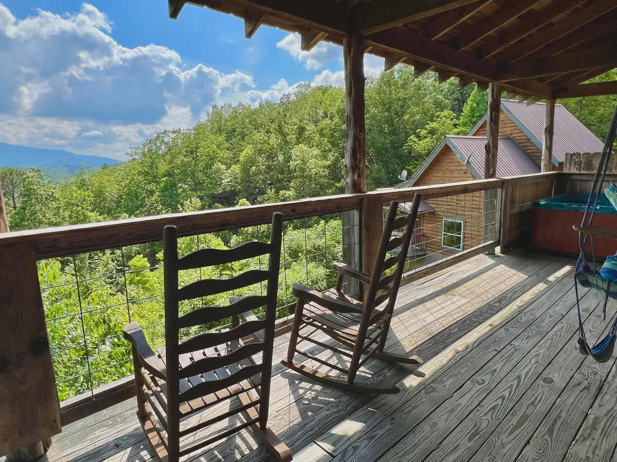 This image showcases a peaceful deck with wooden rocking chairs overlooking a stunning mountain view. The wooden railing frames the expansive vista, inviting guests to sit, relax, and soak in nature. The setting emphasizes tranquility and privacy, ideal for couples seeking a romantic escape.