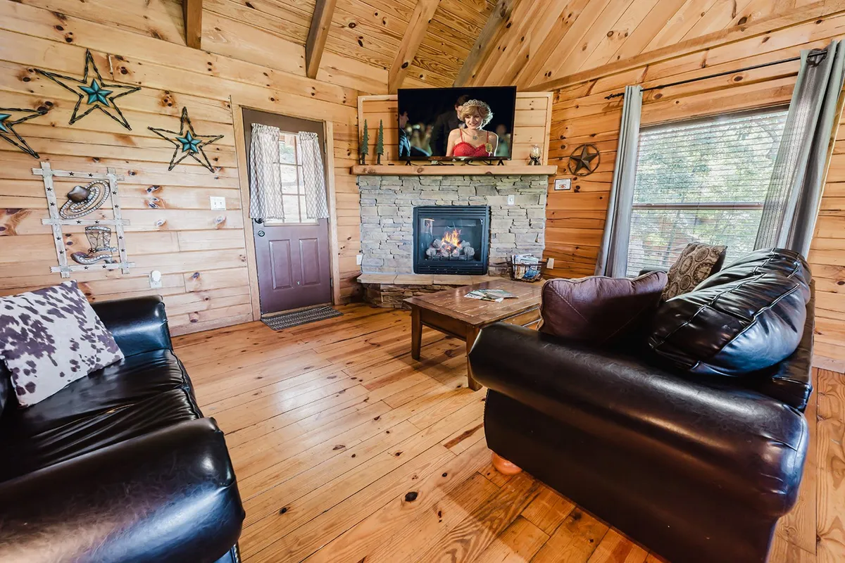 A cozy interior living area features a stone gas fireplace, wooden walls, a comfortable couch, and a coffee table. The atmosphere is warm and inviting, perfect for couples to unwind after a day of exploring, especially during cooler months.