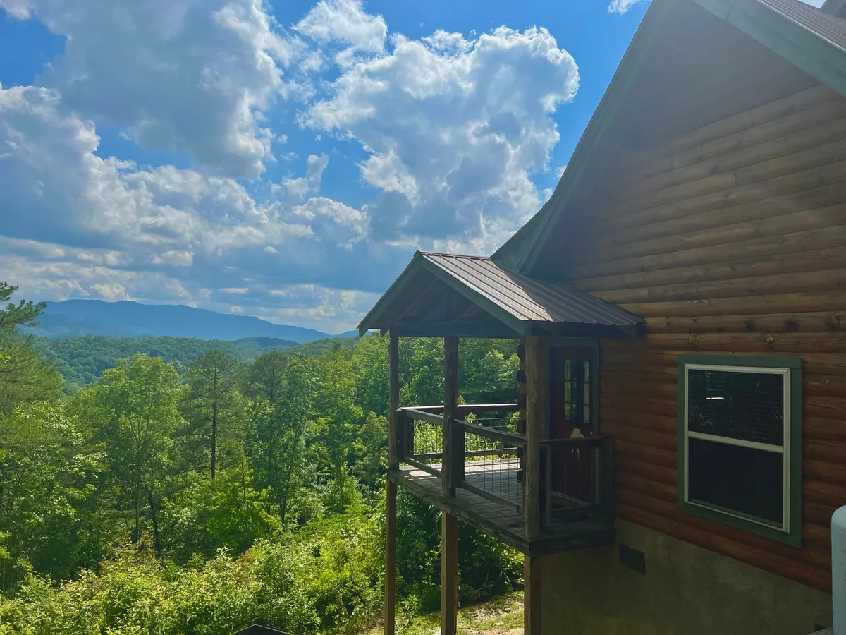 A log cabin with a spacious porch area overlooks breathtaking mountain scenery. The porch invites guests to relax, with ample room for sitting and enjoying the views. The surrounding greenery emphasizes the connection to nature and the cabin’s tranquil setting—perfect for guests looking to explore the outdoors with their pets.