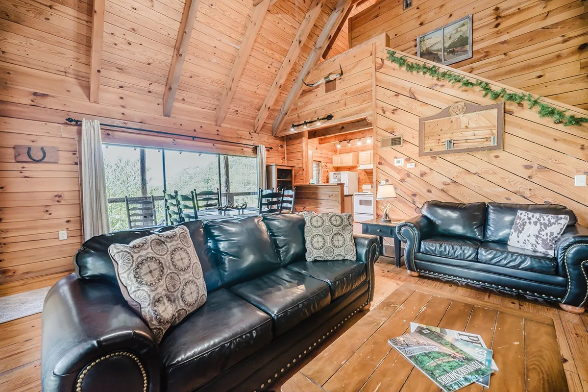 An inviting living area with a leather sofa, rustic wooden beams, a large window bringing in natural light, and tasteful decor. The scene conveys warmth, comfort, and a welcoming atmosphere where guests can relax, socialize, or connect via high-speed WiFi.